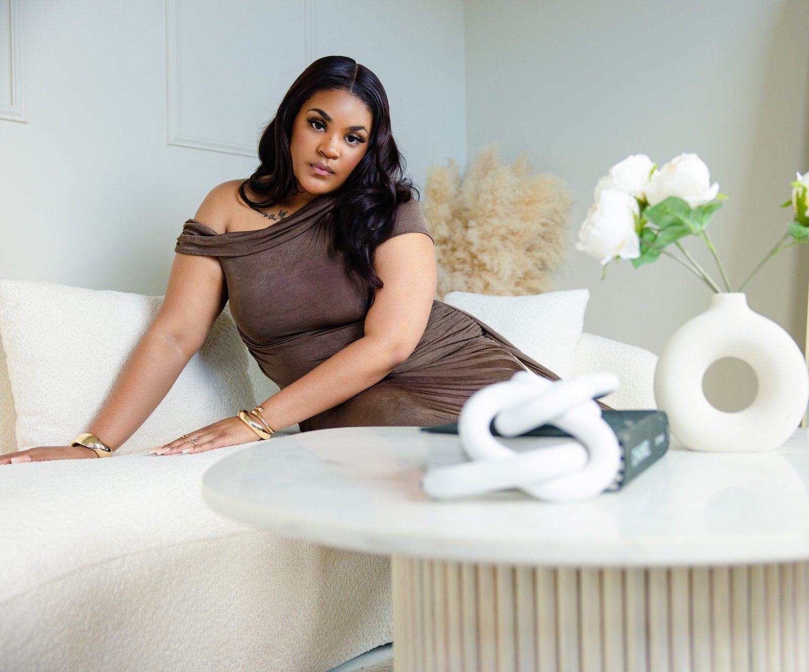 Personal branding portrait of a model in a brown off-shoulder dress posing on a white sofa in a neutral studio