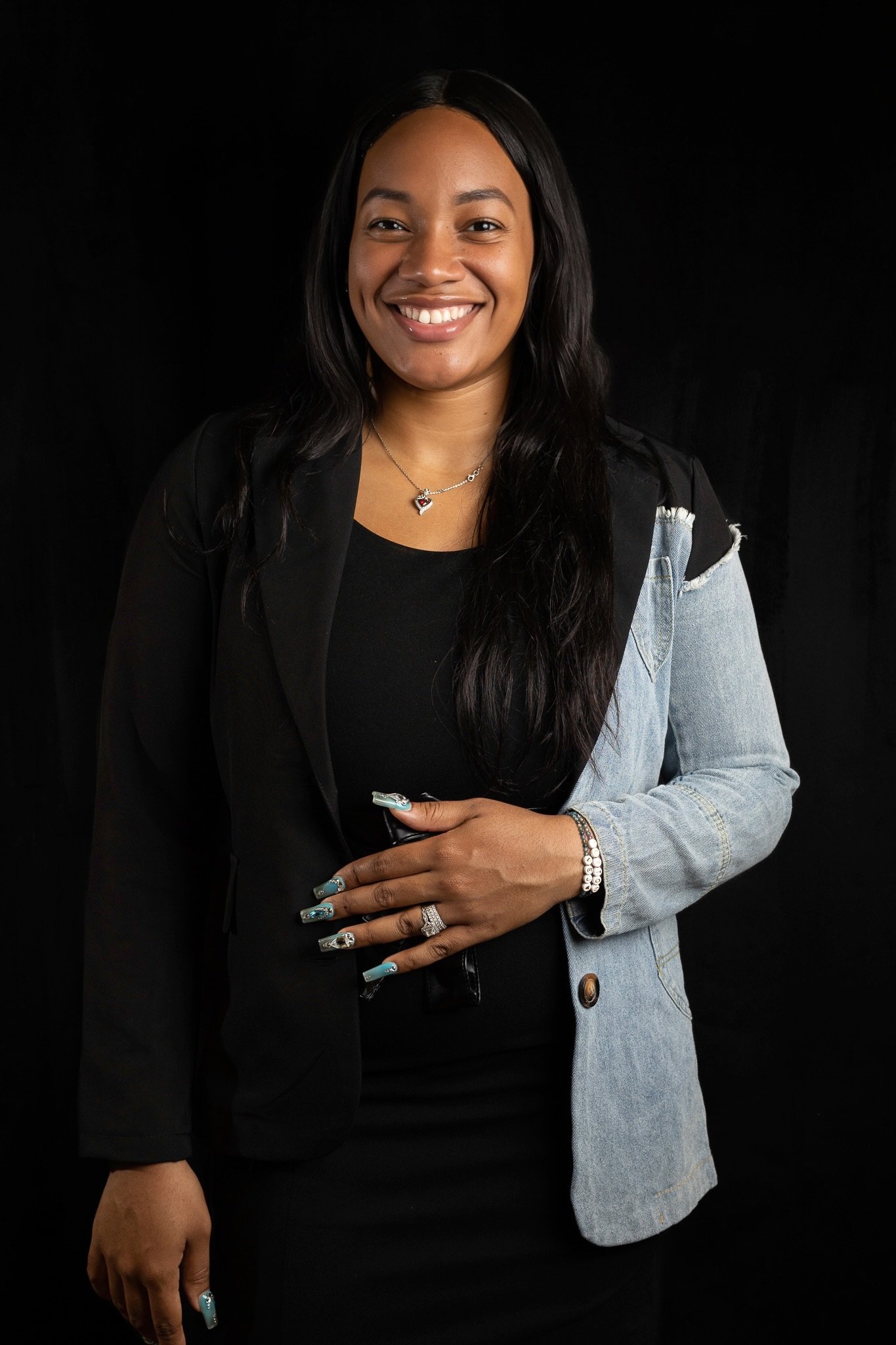 Chelsea of The Christian Doula Experience smiling in a split black-and-denim blazer for a professional headshot against a black backdrop