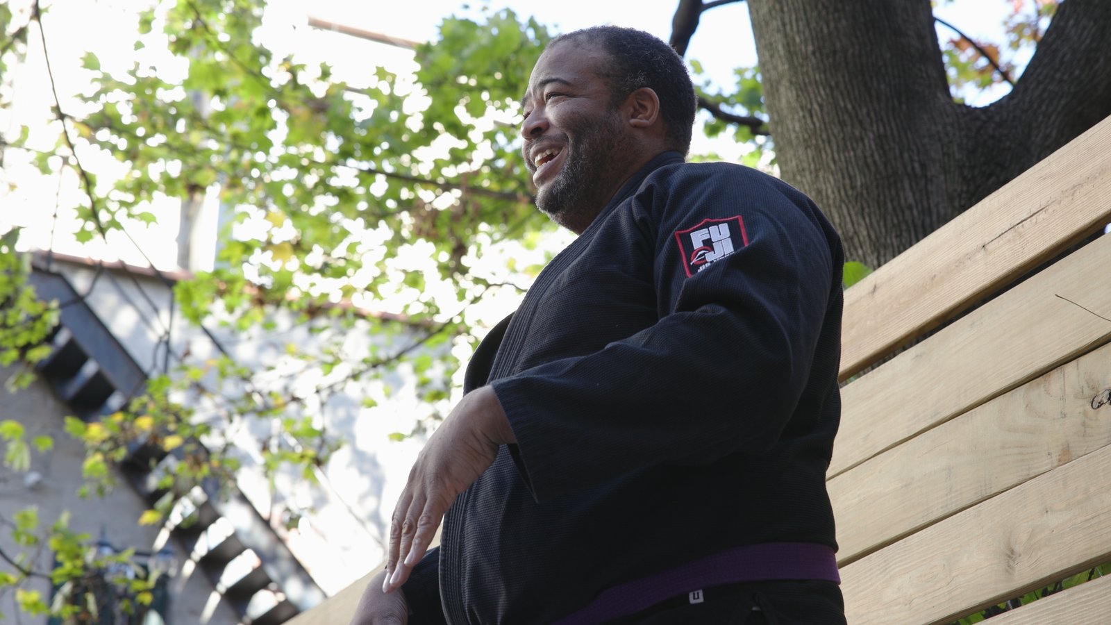 Smiling man in a black gi and purple belt during an outdoor martial arts class, from the Jons Dojo documentary