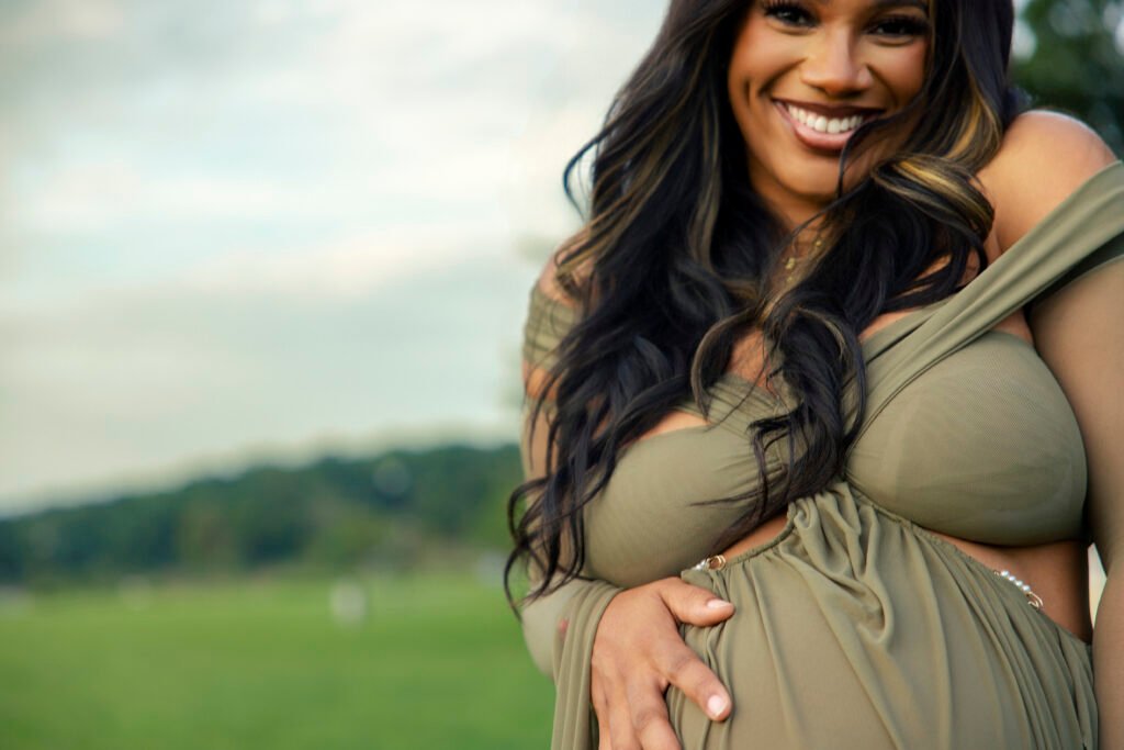 Close-up of a smiling mother-to-be in an olive gown with her hand on her belly at the Mother’s Blessing