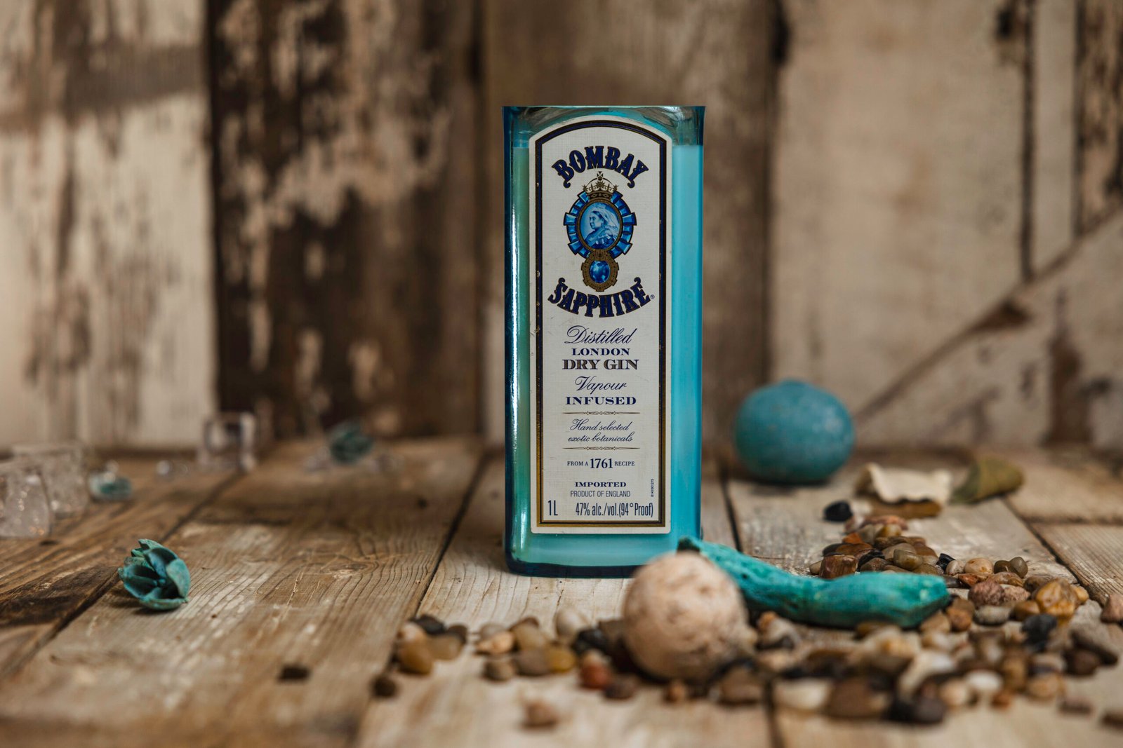 Candle poured into an upcycled Bombay Sapphire gin bottle, styled with river stones on rustic wood for a Bedford, NY candle maker