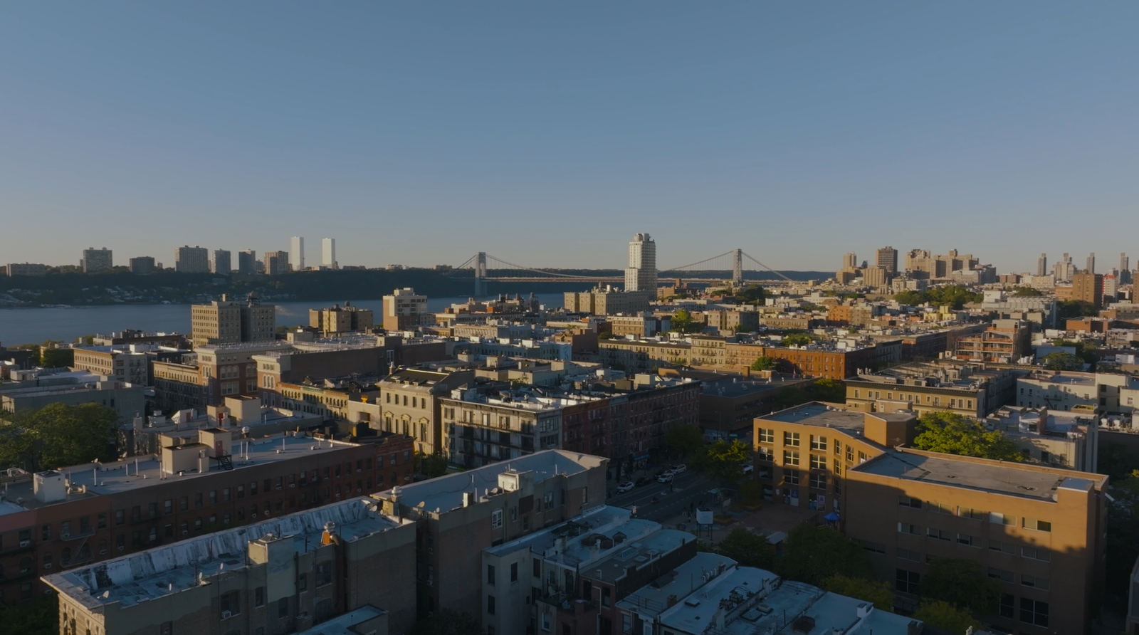 Aerial drone shot of Harlem rooftops at golden hour with the George Washington Bridge and Hudson River in the distance, from the Jons Dojo documentary