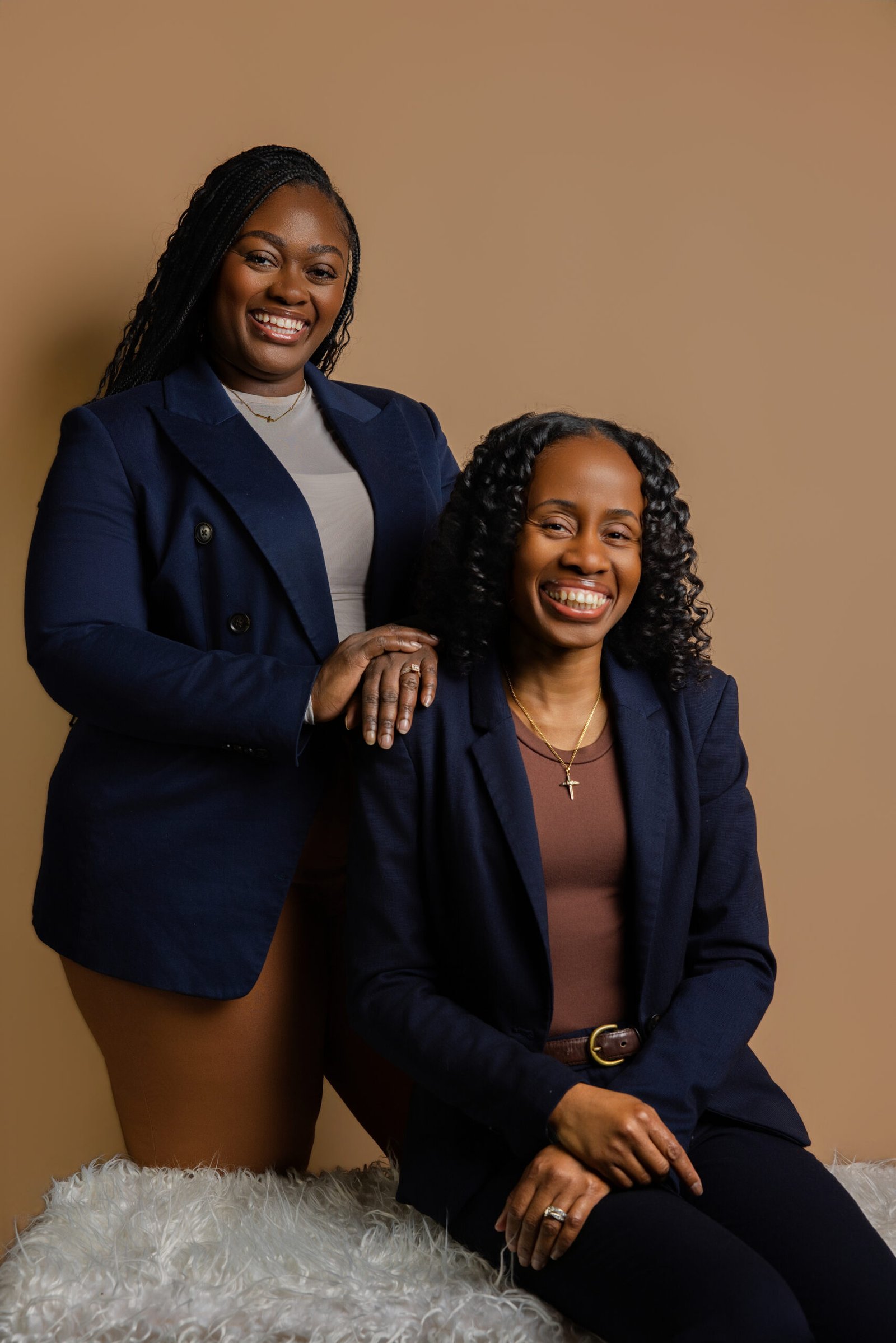 Founders of Sister’s Nursing smiling in navy blazers for a studio branding portrait against a warm tan backdrop