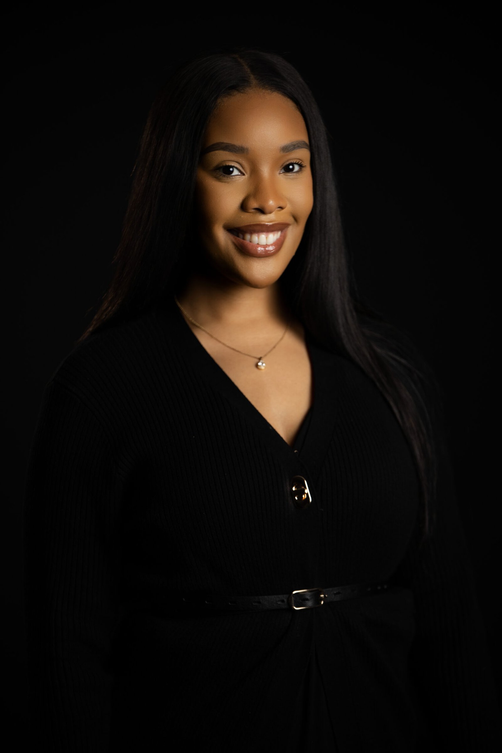 Professional headshot of a smiling woman in a black cardigan against a dark studio backdrop