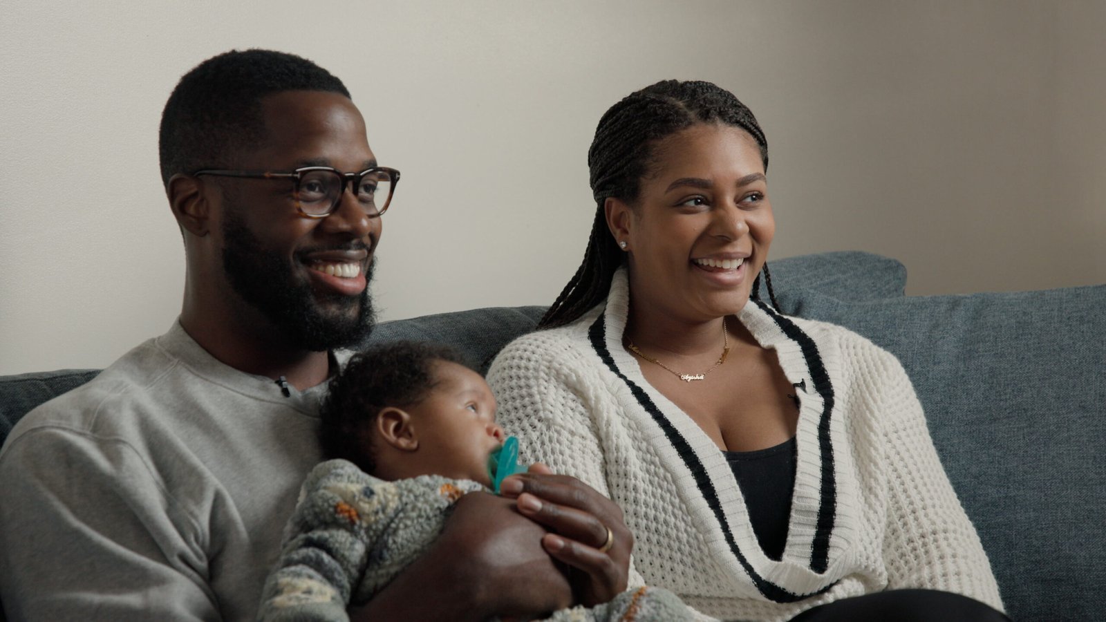Couple smiling on the couch with their newborn during a family documentary interview