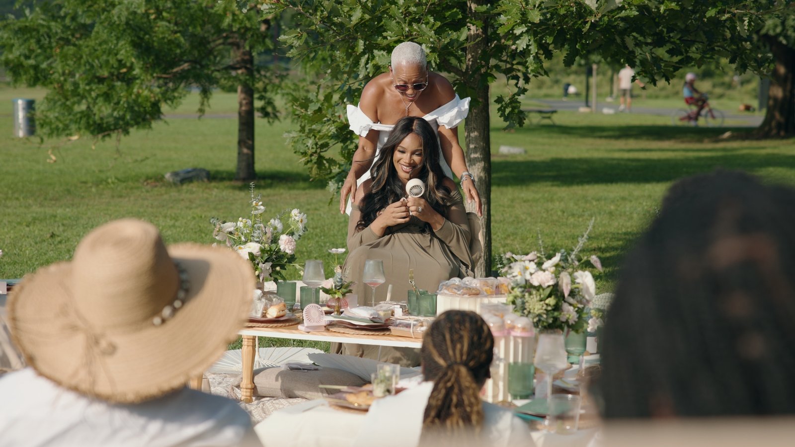 Smiling mother-to-be surrounded by loved ones at an outdoor Mother’s Blessing picnic in the park, hosted by The Christian Doula Experience